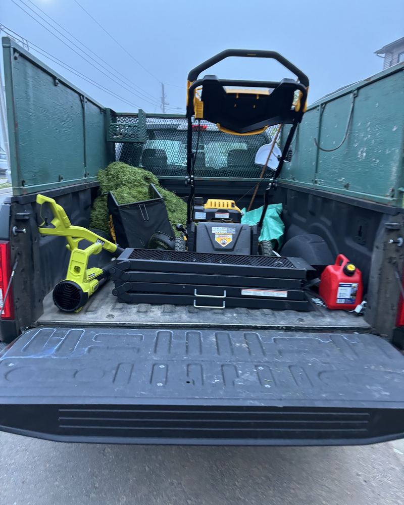 Open tailgate of a pickup loaded with a lawn mower, leaf blower, gas can and bagged clippings