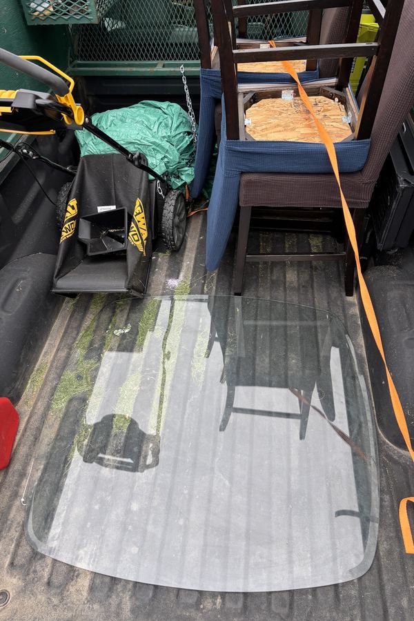 Pickup bed loaded with old wooden chairs, a glass panel and a lawn mower, strapped down for the drive
